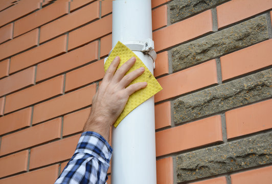 Man Cleaning White Roof Gutter Downspout Pipe.