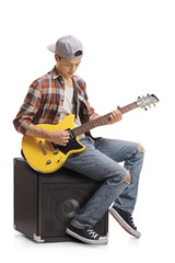 Teenager with an electric guitar sitting on an amplifier and playing
