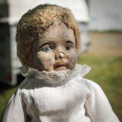 Old worn vintage doll, with white dress and lace, and broken nose