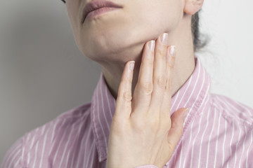 A sore throat. A woman holds her hand to her neck. Angina.