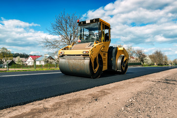 yellow road roller makes new asphalt