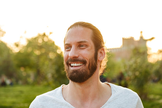 Profile Closeup Of Cheerful Happy Man 30s With Tied Hair In White T-shirt Laughing With Beautiful Smile, While Resting In Green Park