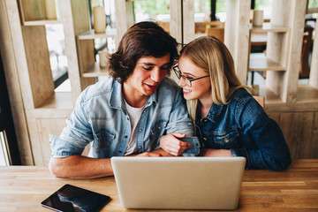 Young charming couple using laptop while sitting at cafe