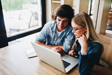 Young charming couple using laptop while sitting at cafe