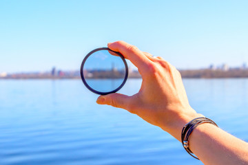 Female hand with a photo filter on the background of the lake and the city