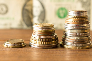 Three stacks of different coins on the background of 1 dollar bill .