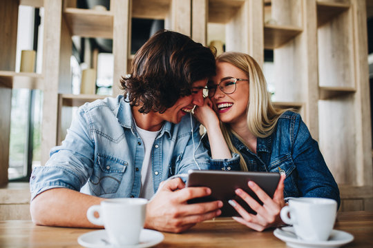 Young Charming Couple Using Tablet While Sitting Together And Drinking Coffee