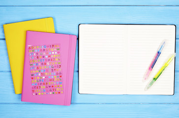 Top view of pink and yellow notebook,abc alphabet letters and colorful pens on a blue wooden desk background with blank sheet for copy space text. Back to school concept. Close up, minimal flat lay.