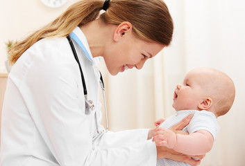 Young joyful doctor holding baby girl and smiling in hospital.  - 207297153