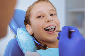 Perfect smile. Cheerful girl turning her head while staring at dentist, treating caries