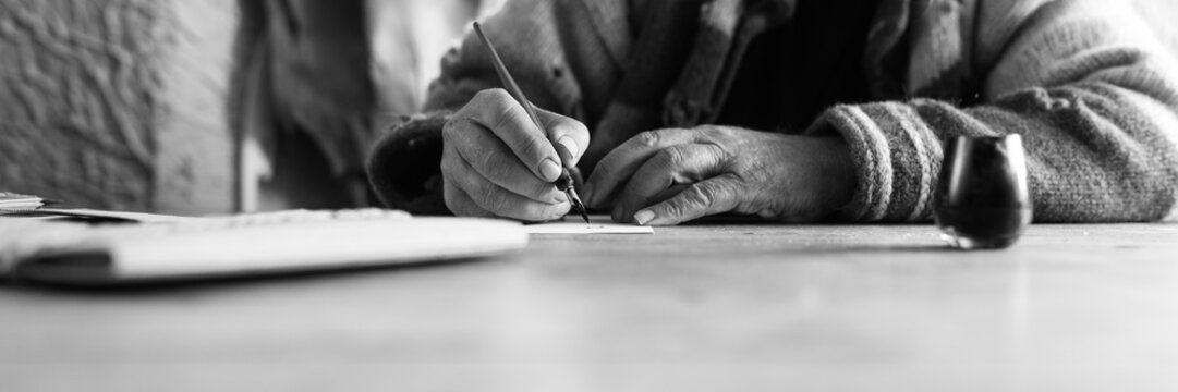 Wide low angle view of an elderly man doing calligraphy writing using a nib pen and ink