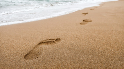 Close up of footprints in wet sand on the beach at sunset. Concept for traveling to tropical / exotic places, vacation and holiday.