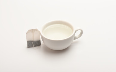 Mug filled with boiling water and teabag on white background. Process of tea brewing in ceramic mug. Tea time concept. Cup or white porcelain mug with transparent hot water and dry bag of tea near