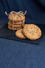 homemade oat cookies with sunflower seeds on shale board and dark blue textile background