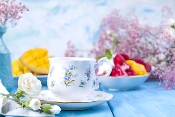 A cup of fragrant morning coffee, fruit ice cream and and flowers are white and pink on a blue wooden background. Vintage photo.