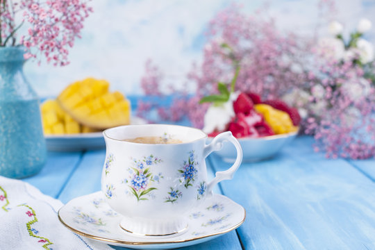 A cup of fragrant morning coffee, fruit ice cream and and flowers are white and pink on a blue wooden background. Vintage photo. Copy space
