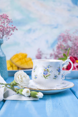 A cup of fragrant morning coffee and flowers are white and pink on a blue wooden background. Vintage photo. Copy space.