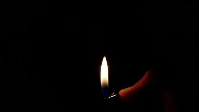 Close up of the hand holds an inflamed lighter on a black background
