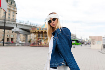 Naklejka premium Fashion outside portrait of young female model with blond hair posing with denim jakcet and black sunglasses in the city