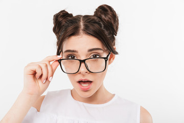 Fototapeta premium Photo closeup of surprised teenage girl 20s with double buns hairstyle and dental braces touching eyeglasses with curious look, isolated over white background
