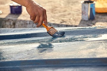 Man painting boat.Closeup view of hand holding a paintbrush with blue color.