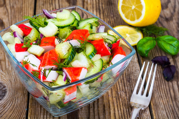 Vegetable salad with crab sticks in glass salad bowl on wooden table
