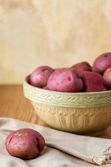 Fresh, Raw, Red Potatoes in a Vintage Bowl on a Wood Table with Yellow Plaster Wall in the Background
