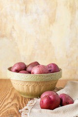 Fresh, Raw, Red Potatoes in a Vintage Bowl on a Wood Table with Yellow Plaster Wall in the Background