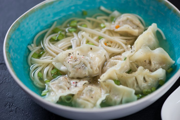 Blue bowl of noodle soup with wontons, selective focus, closeup, horizontal shot