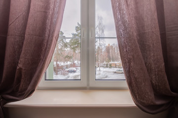Home window with brown curtain and view to the winter back-front yard.