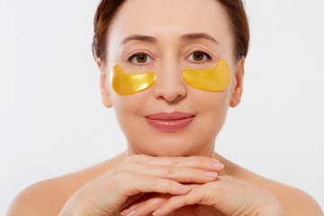 Macro female face. Beauty portrait of middle age woman with wrinkles and a gold patch under eye isolated on white background. Collagen mask and spa concept. Copy space. Seasonal skin care