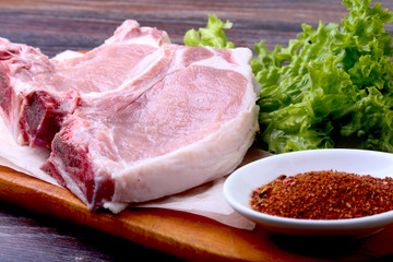 Raw pork steak with spices Leaves lettuce on wooden cutting board. Ready for cooking.
