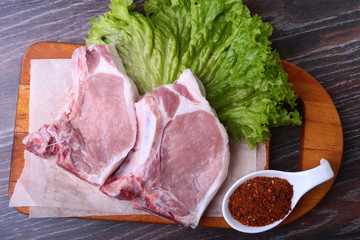Raw pork steak with spices Leaves lettuce on wooden cutting board. Ready for cooking.