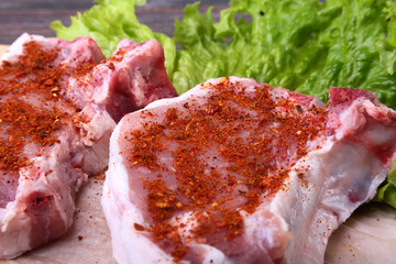 Raw pork steak with spices Leaves lettuce on wooden cutting board. Ready for cooking.