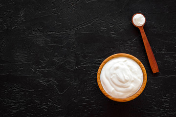 Healthy product, healthy meal. Greek yogurt in brown bowl near spoon on black background top view copy space