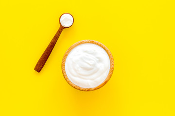 Healthy product, healthy meal. Greek yogurt in brown bowl near spoon on yellow background top view copy space