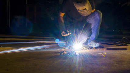 worker welding metal, focus on flash light line of sharp spark,in low light