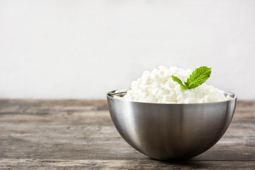 Fresh cottage cheese in a metal bowl on wooden table. Copyspace