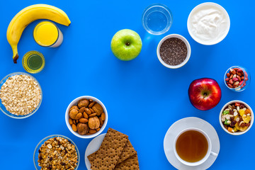 Make a menu for wholesome breakfast. Fruits, oatmeal, yogurt, nuts, crispbreads, chia on blue background top view copy space