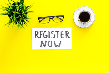 Membership concept. Template for registration. Register now hand lettering iconon word desk with glasses, coffee, plant on yellow background top view space for text