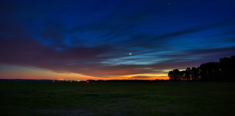 Venus in the night sky with stars. A bright sunset with clouds. Cosmic space above the earth's surface. Long exposure. © olgapkurguzova