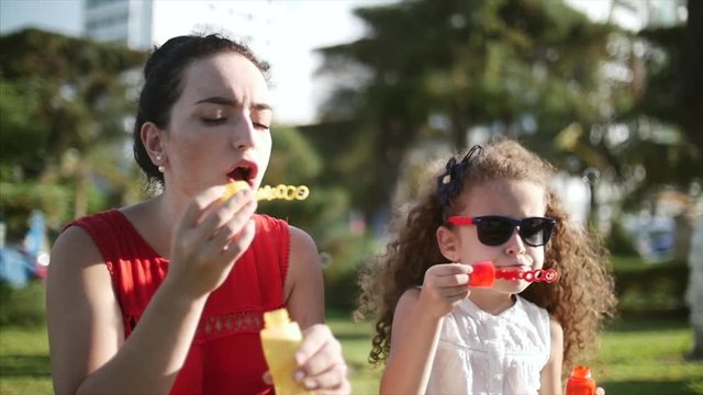 Happy mam and child blowing soap bubbles in park. Slow motion. Stock footage. Slow motion