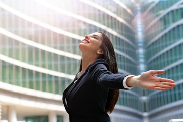 An asian business woman, dressed in a suit, raises her arms to the sky and breathes as a sign of...