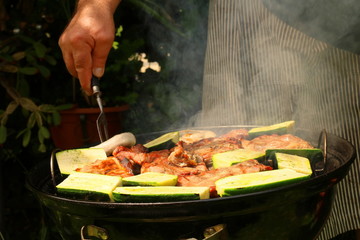 Ein Mann grillt im Garten am Kugelgrill Fleisch und Gemüse