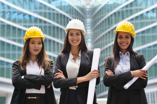 Three engineer women of different ethnicities (Asian, European and African American) with helmets watch a construction project and discuss how to continue the work. Concept of: construction, team