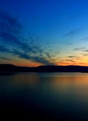 Fototapeta na wymiar Orange sunrise reflect in dark calm water surface of lake Baikal early morning. Summer landscape sunrise over water with silhouette mountain range on another shore lake