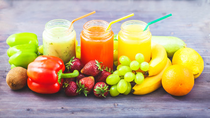 freshly squeezed fruit juice, smoothies yellow orange green blue banana lemon apple orange kiwi grape strawberry on a dark wooden background Copy space
