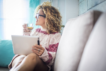 beautiful 40 years old middle age woman cacuasian curly long hair at home working at tablet white look outside the window. water with lemon to have care of her body and wellness beauty. relaxed 