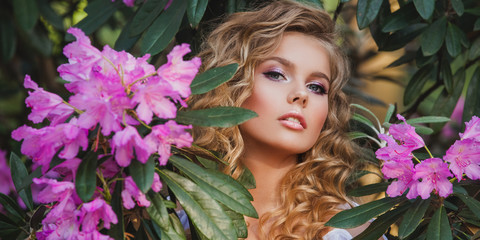 Portrait of a girl in a blooming garden. A bush of flowers is rhododendron pink. Beautiful hair and makeup.