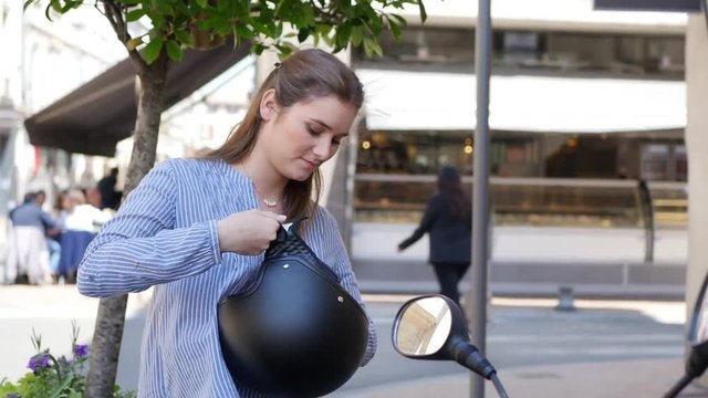 attractive young woman in a modern city adjusting motorcycle helmet in summer